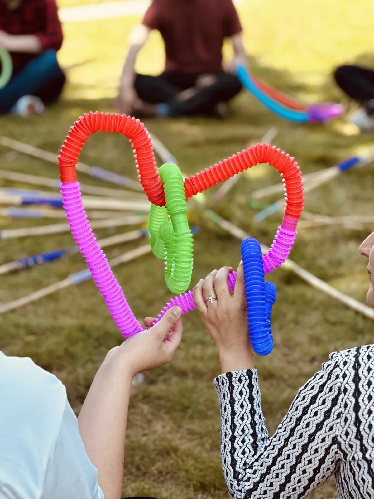 Personas construyendo una figura con tubos de colores sobre el pasto