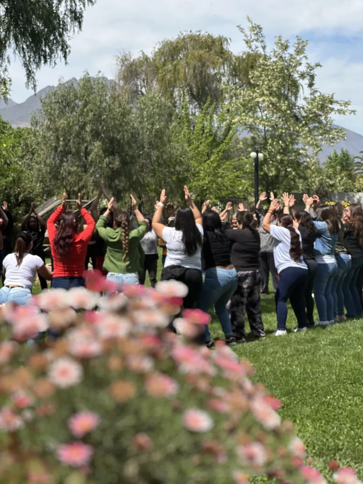 Círculo de personas con los brazos en alto en un jardín, con la cordillera de fondo
